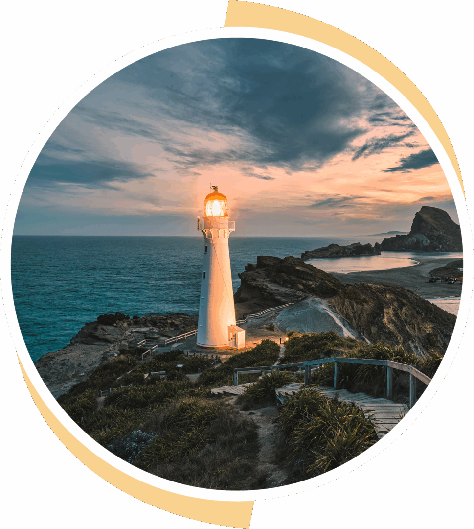 A lighthouse standing tall on rocky shores at sunset.